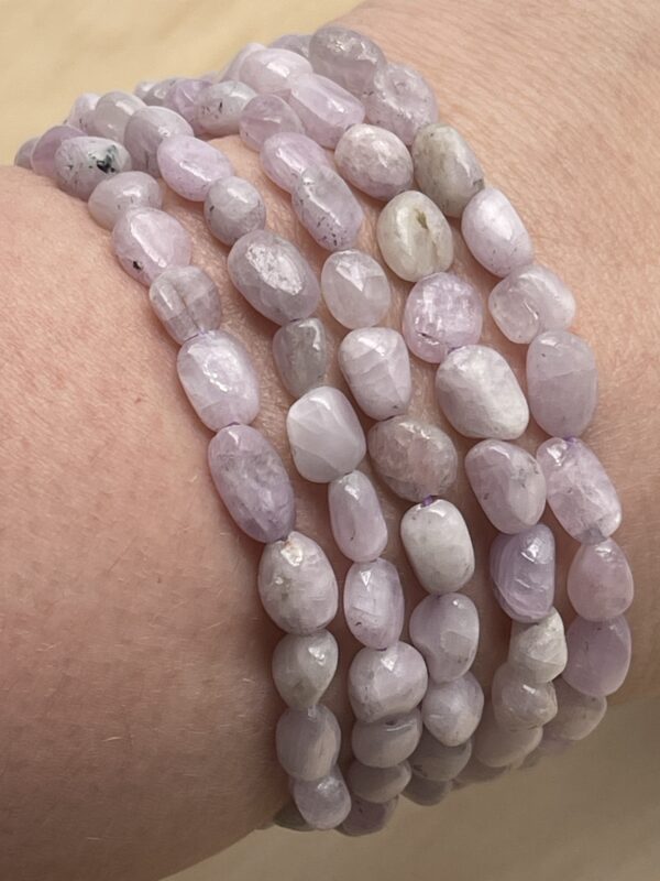 Plusieurs bracelets en kunzite naturelle enroulés au poignet – nuances douces et pierres lumineuses.